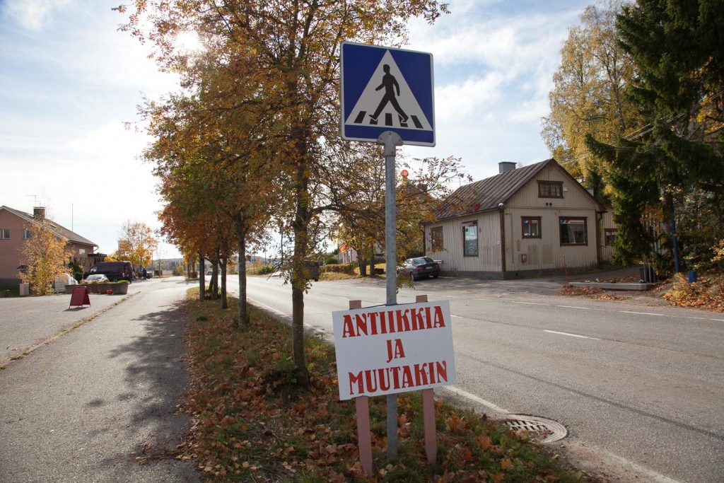 Kylänraitti, jonka varrella koivuja, rakennus ja etualalla kyltti jossa lukee Antiikkia ja muuta.