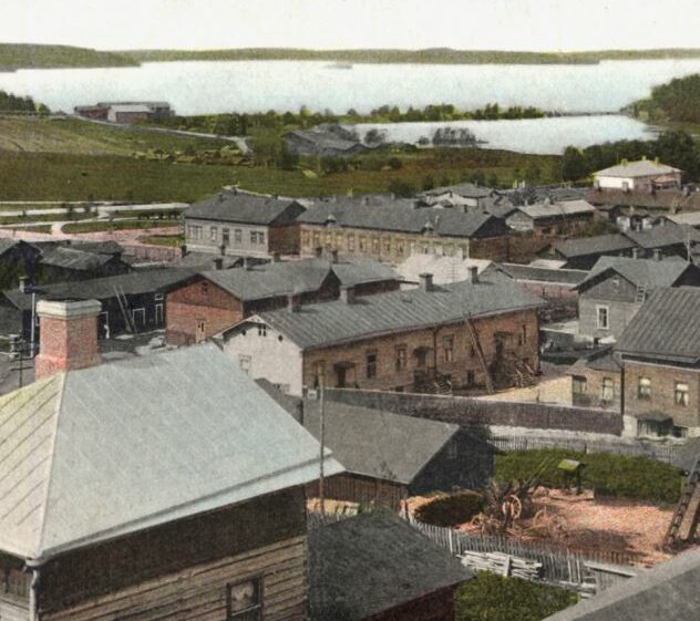 Yksityiskohta kirjankansikuvasta jossa rakennuksia ja taustalla järvi.