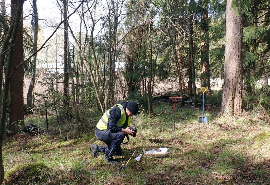 polvistunut mies valokuvaa metsikössä maasta tehtyä löytöä.