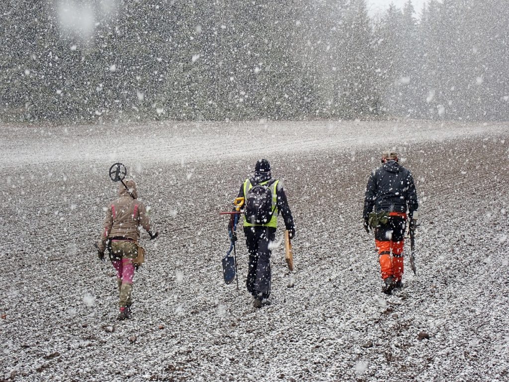 Arkeologit kävelevät pellolla sankassa lumisateessa.