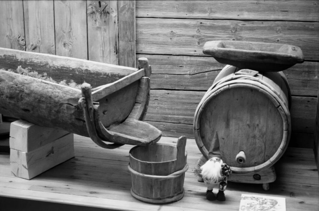 Pöytätasolla sahdinteossa käytetty puinen kuurna, puutynnyri ja puinen kimpiastia. Puutynnyrin edessä pieni käsintehty tonttuhahmo