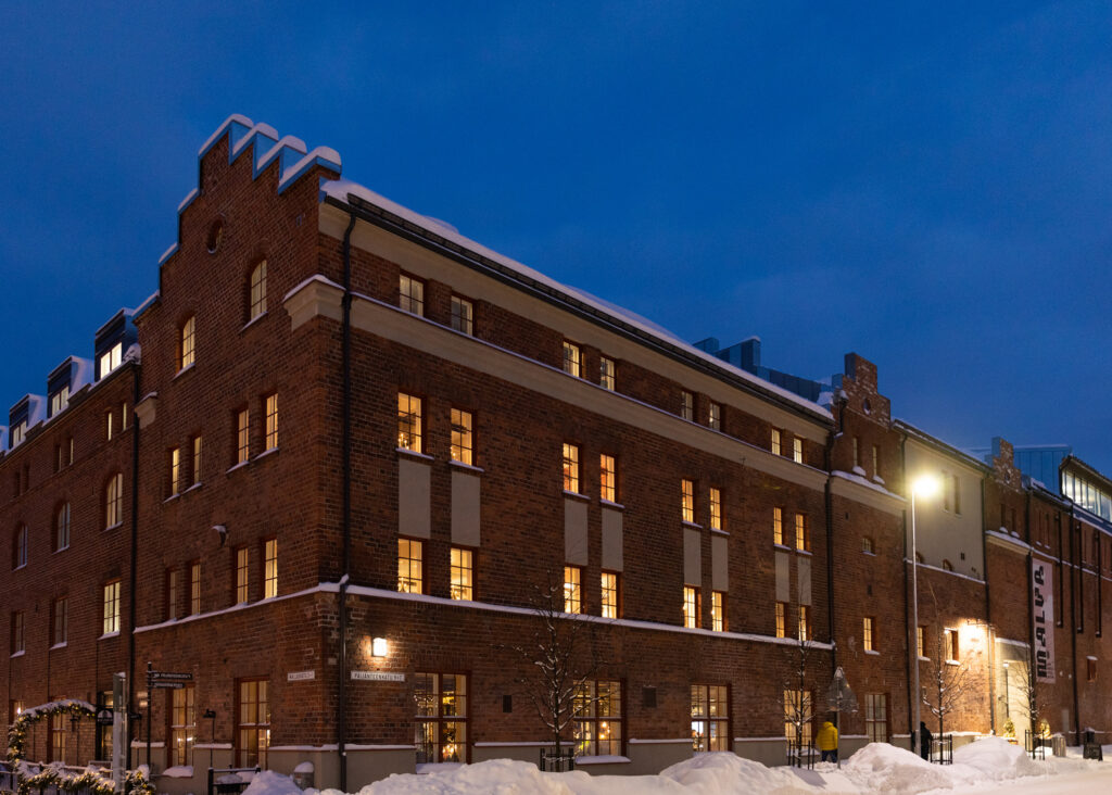 Punatiilinen vanha tehdasrakennus valaistuna hämärtyvässä talvi-illassa.